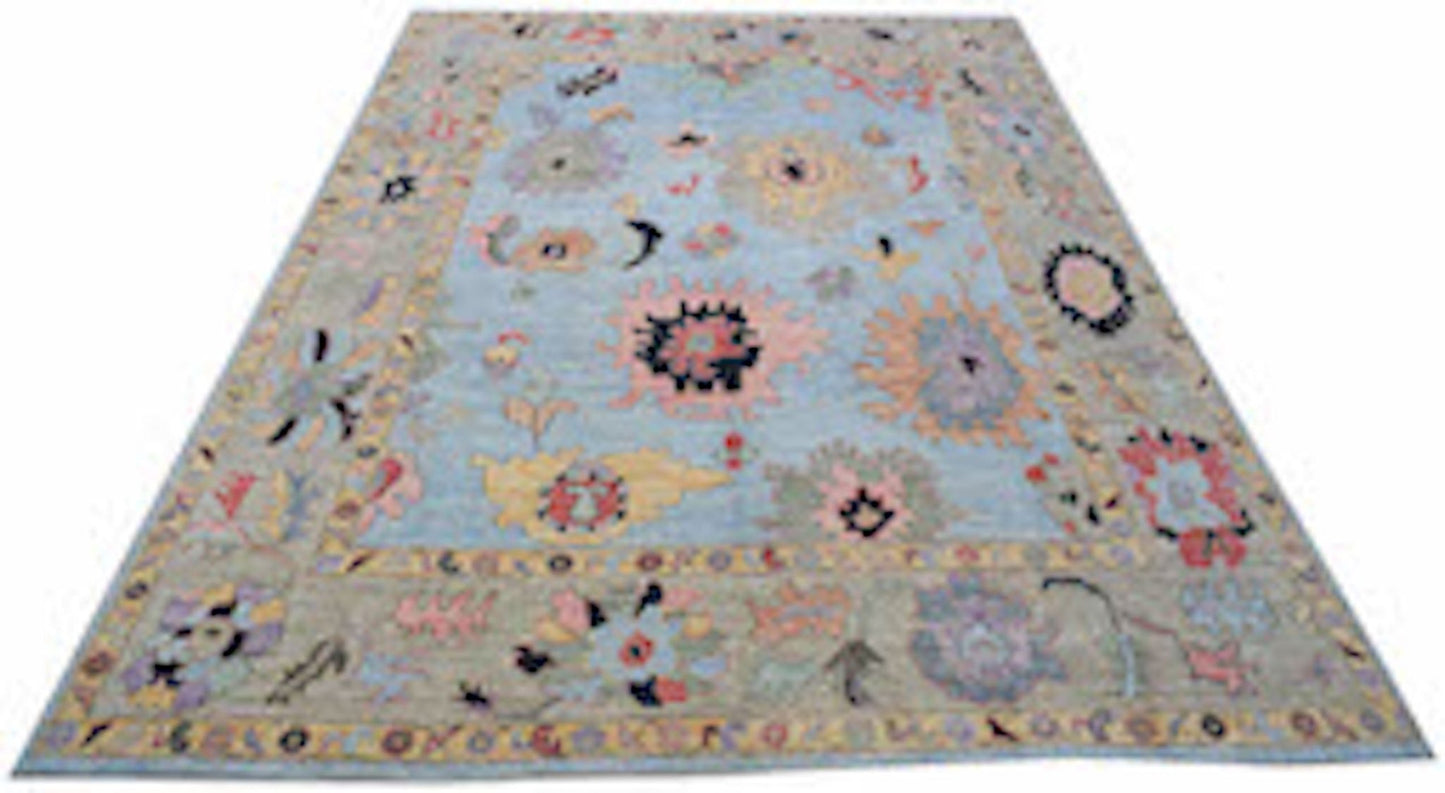A handwoven transitional Oushak rug featuring a light blue field with colorful floral motifs.