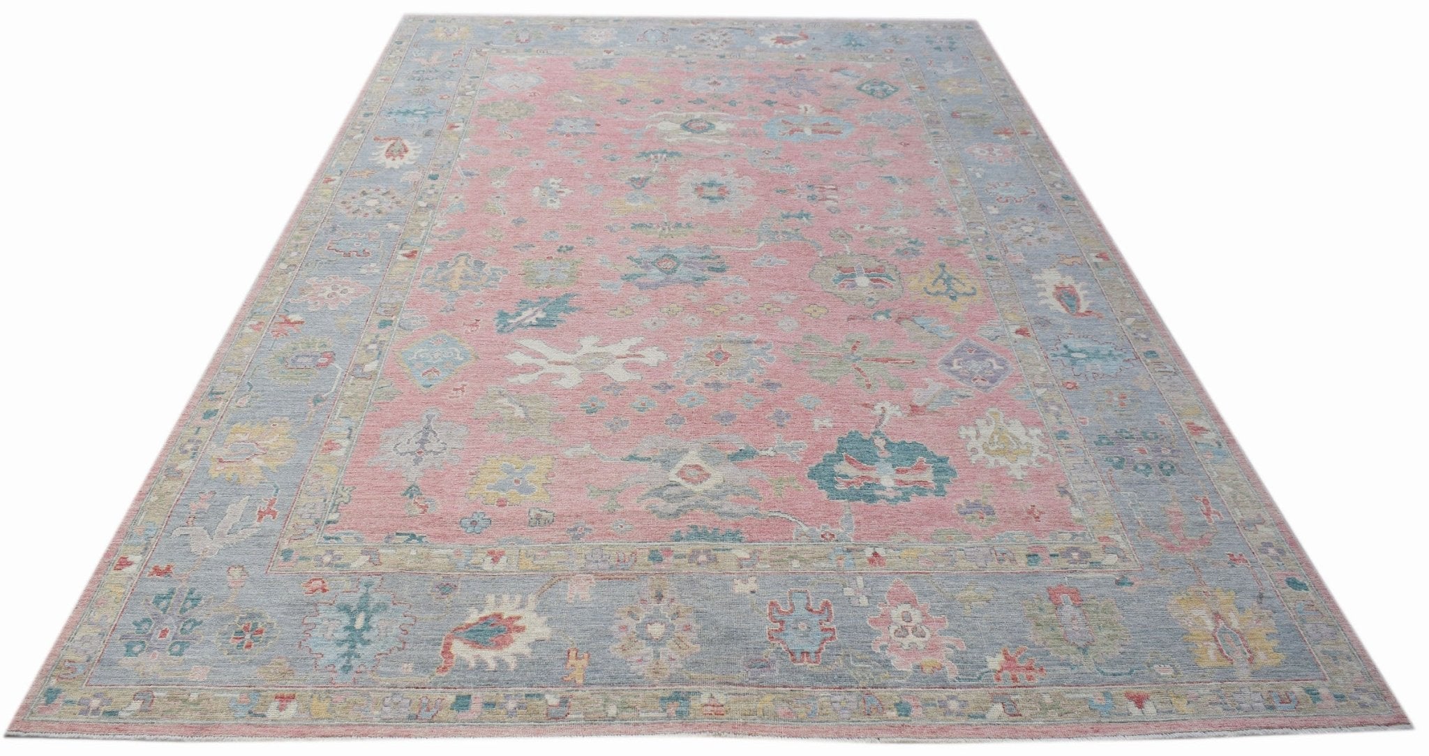 A handwoven transitional Oushak rug featuring a floral pattern in pink and blue tones.