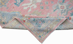 A handwoven transitional Oushak rug featuring a floral pattern in pink, blue, and neutral tones.