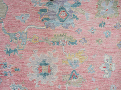 A handwoven transitional Oushak rug featuring a floral pattern in muted tones on a pink background.