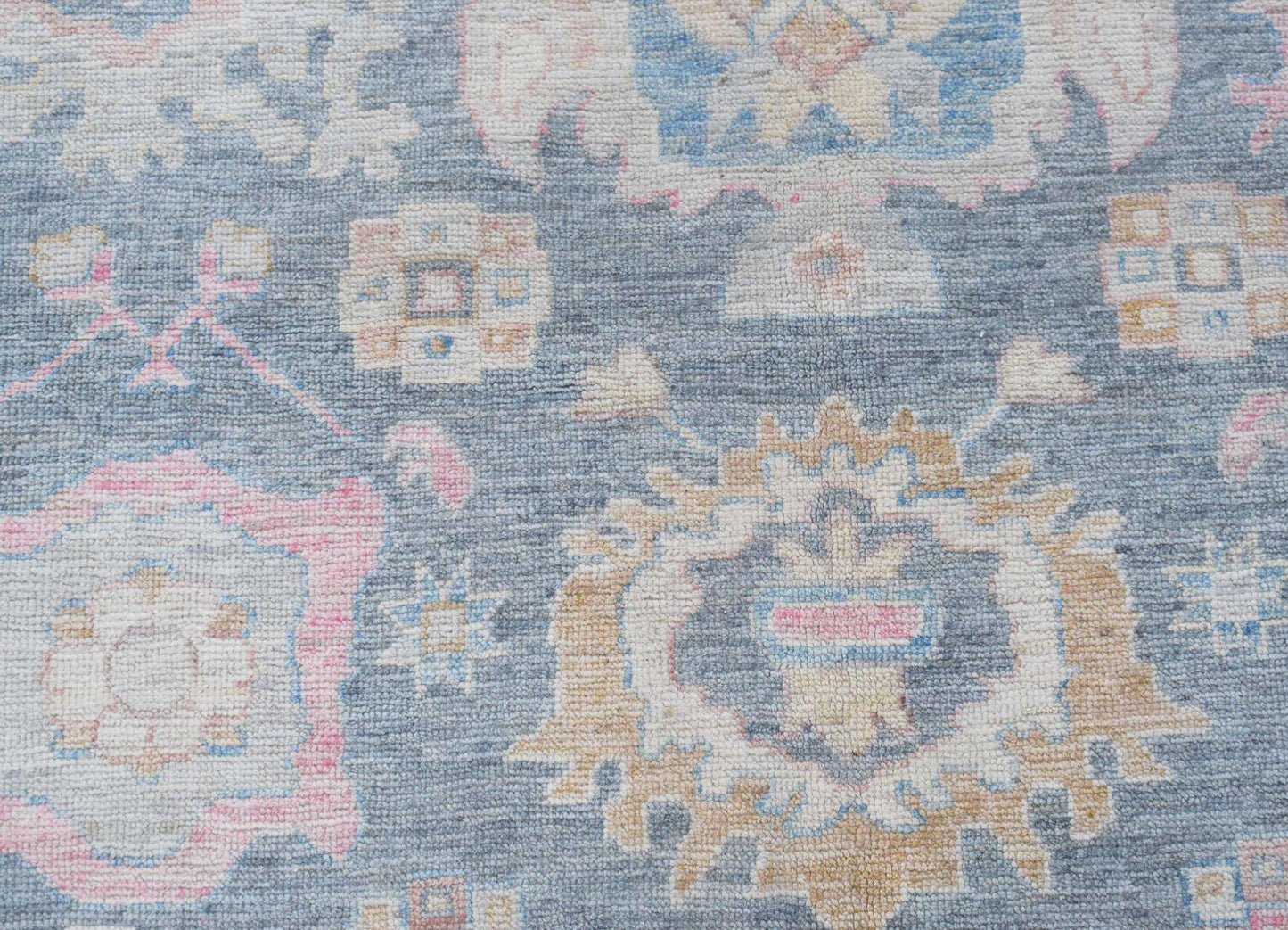 A handwoven transitional Oushak rug featuring a floral pattern in blue, pink, and tan tones.