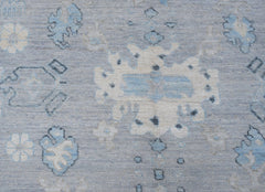 A transitional Oushak rug featuring a light blue field with cream and grey floral motifs.