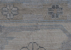 A close-up of a handwoven wool rug featuring a neutral beige background with subtle blue linear accents and geometric motifs.