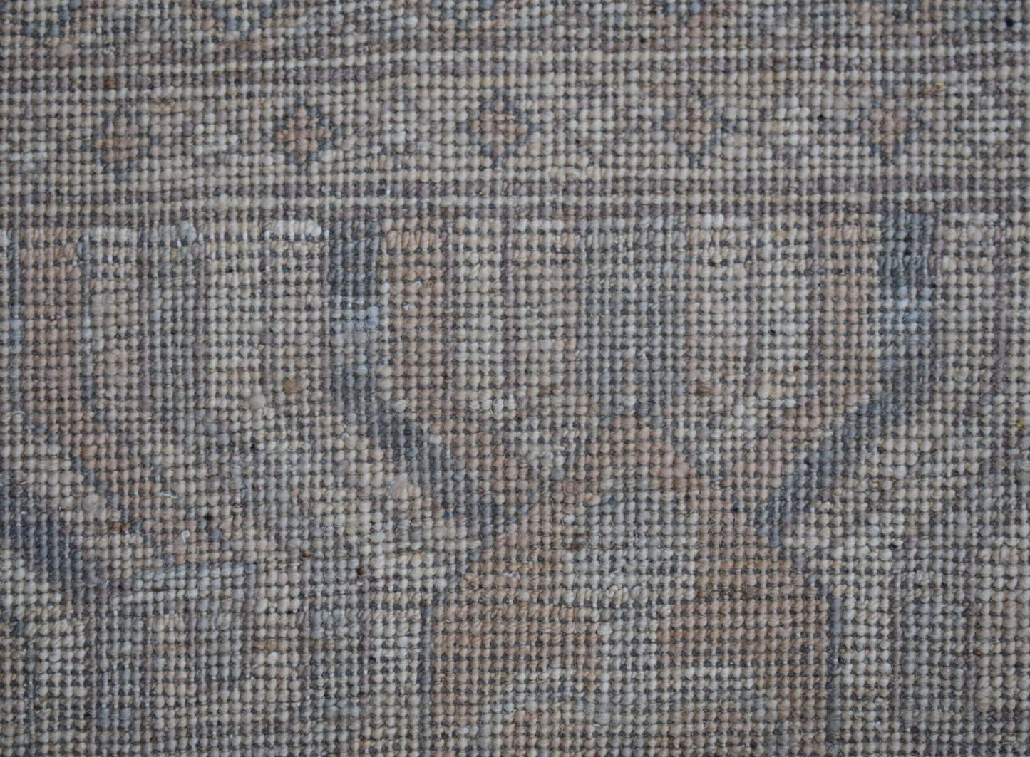 A close-up view of a handwoven wool rug featuring a muted, transitional floral pattern.
