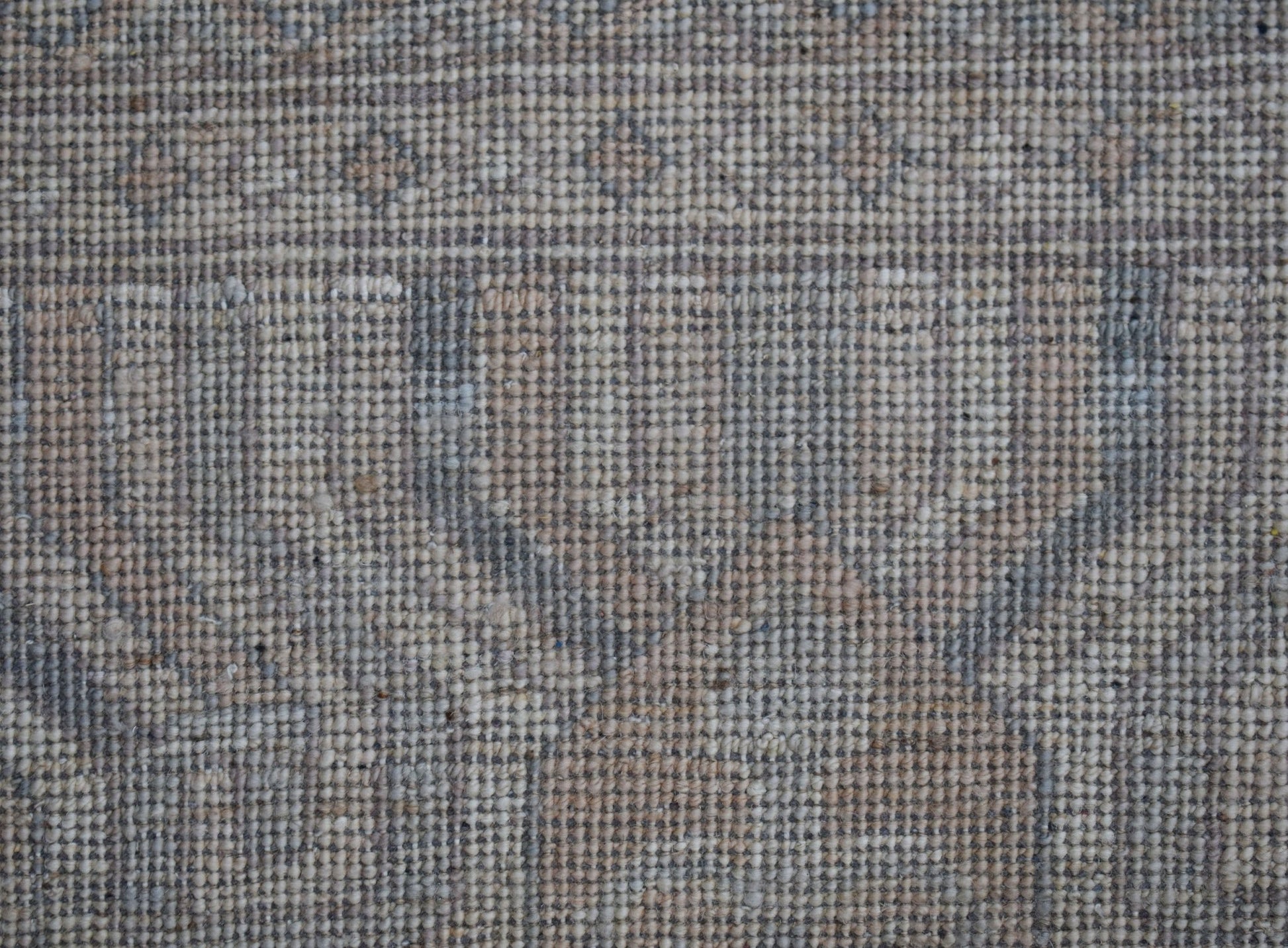 A close-up view of a handwoven wool rug featuring a muted, transitional floral pattern.