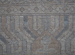 A close-up view of a handwoven wool rug featuring a muted, transitional floral pattern.