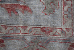A close-up of a handwoven Oushak rug featuring a traditional floral pattern in red and grey tones.