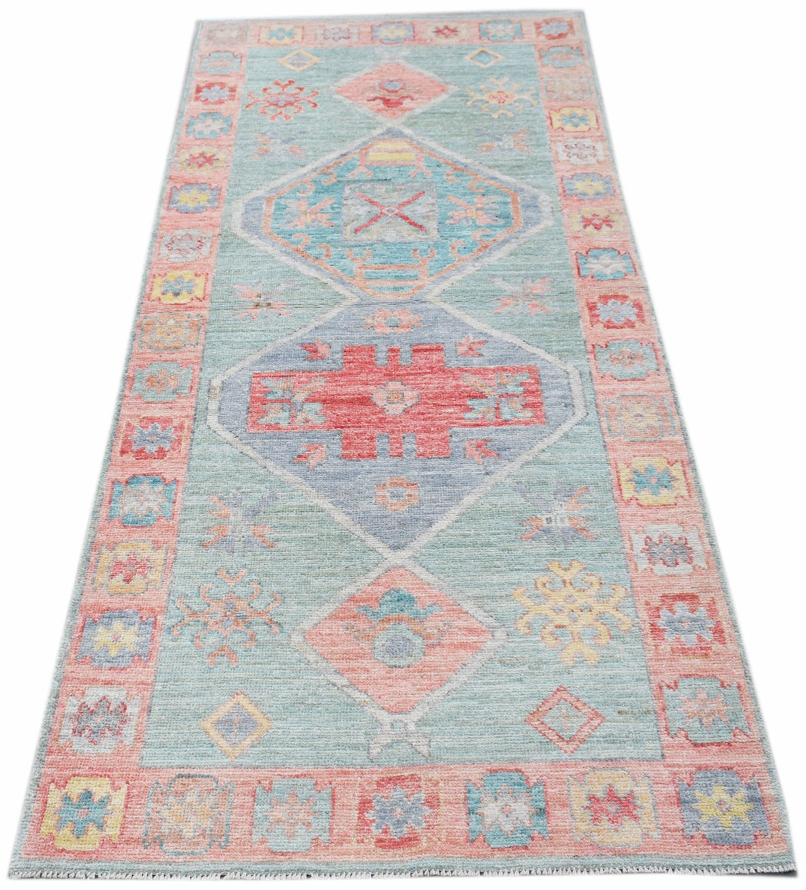 A handwoven wool runner rug featuring a transitional Oushak pattern in soft blue and pink tones.