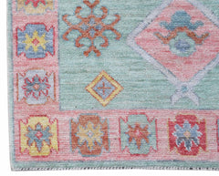 A handwoven wool runner featuring a light blue field with pink borders and geometric floral motifs.