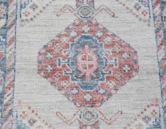 A handwoven wool runner rug featuring a central floral medallion in muted pink and blue tones.