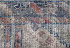 A close-up of a handwoven wool runner rug featuring a transitional floral pattern in muted tones.