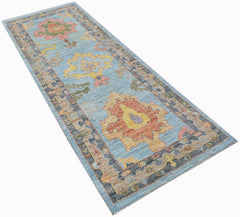 A handwoven wool runner rug featuring a light blue field with colorful floral Oushak patterns.