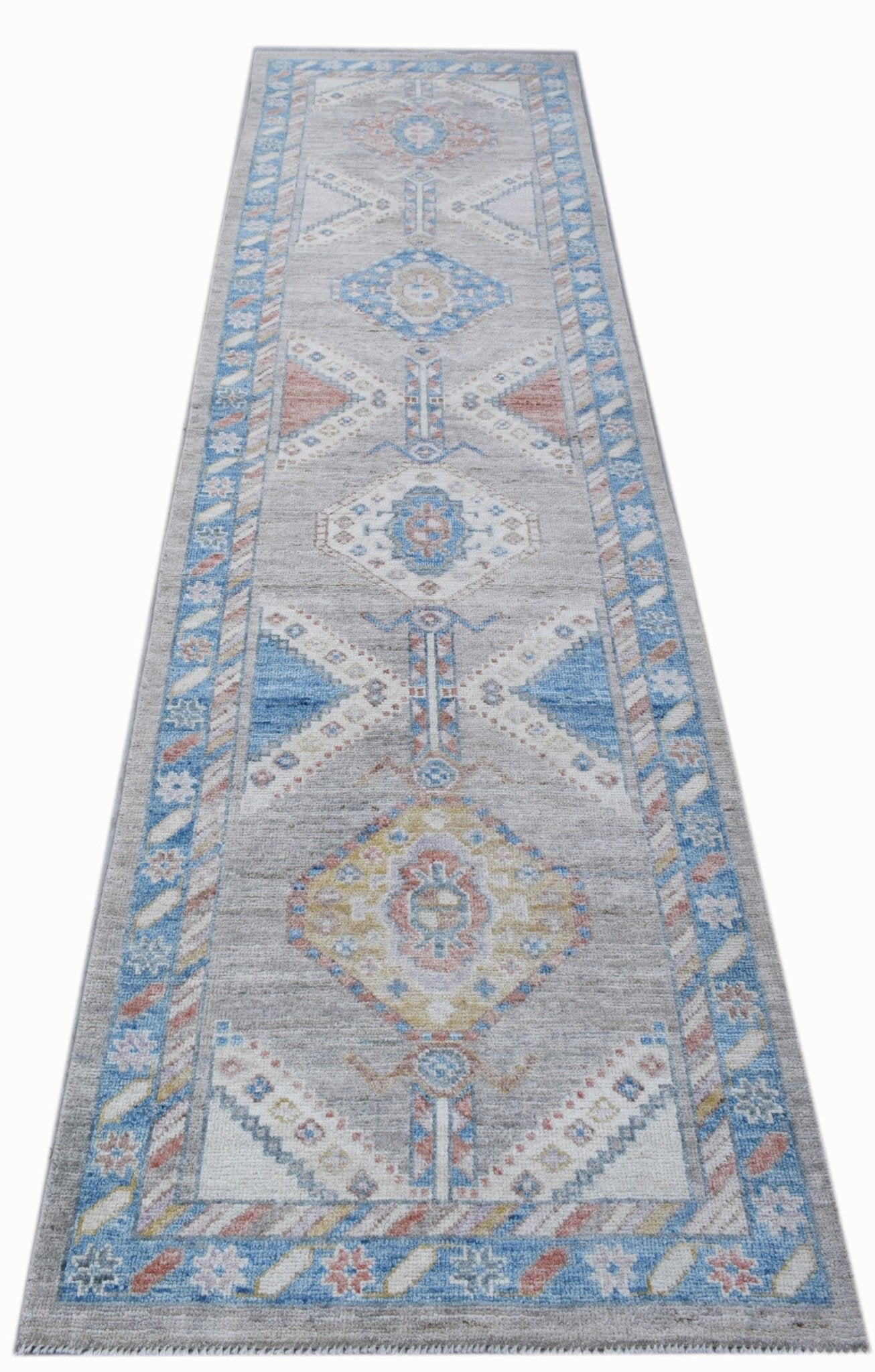A handwoven wool runner rug featuring a transitional Oushak pattern in blue, grey, and yellow.