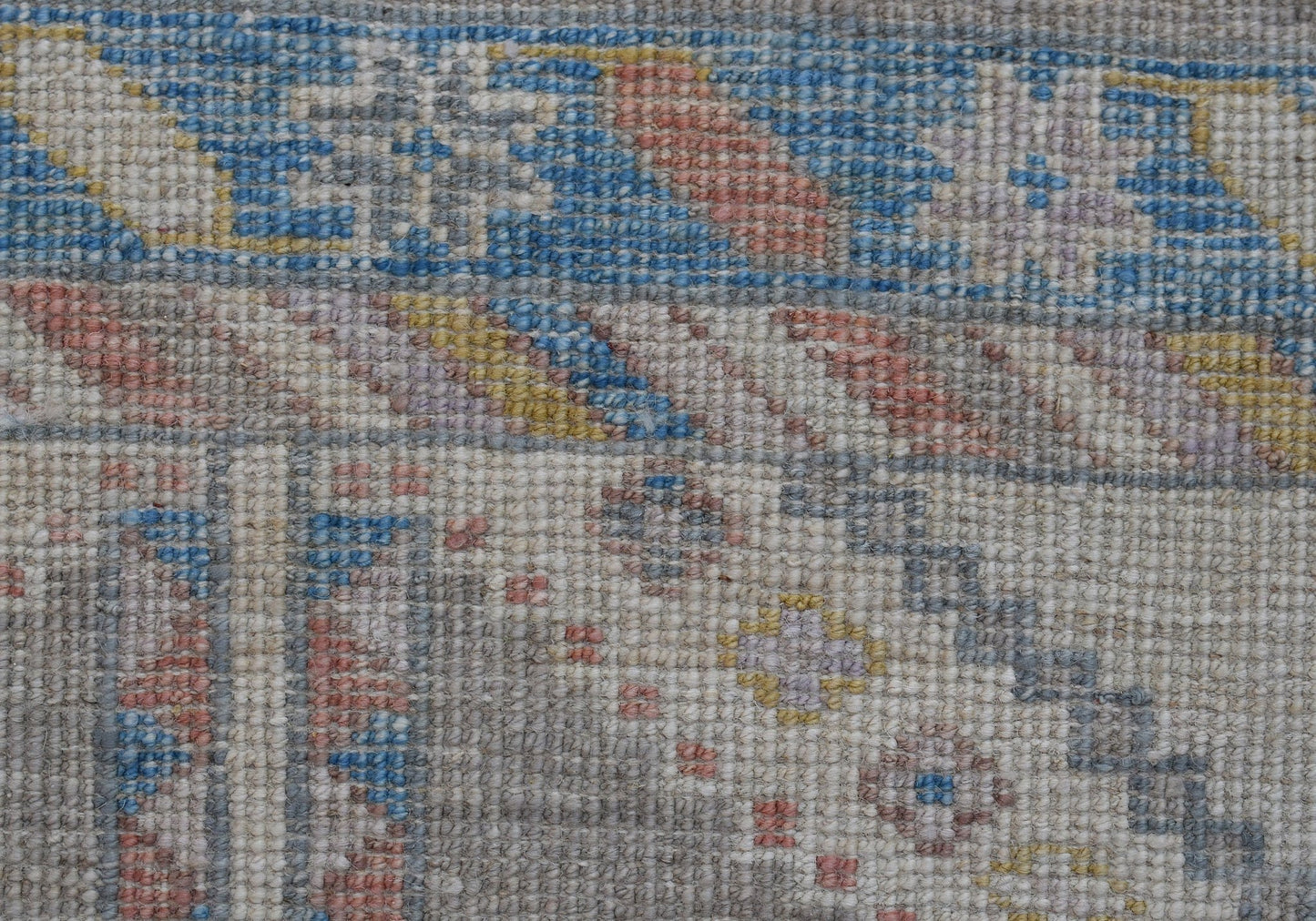 A close-up of a handwoven transitional Oushak runner featuring a geometric floral pattern in blue, pink, and yellow on a neutral background.