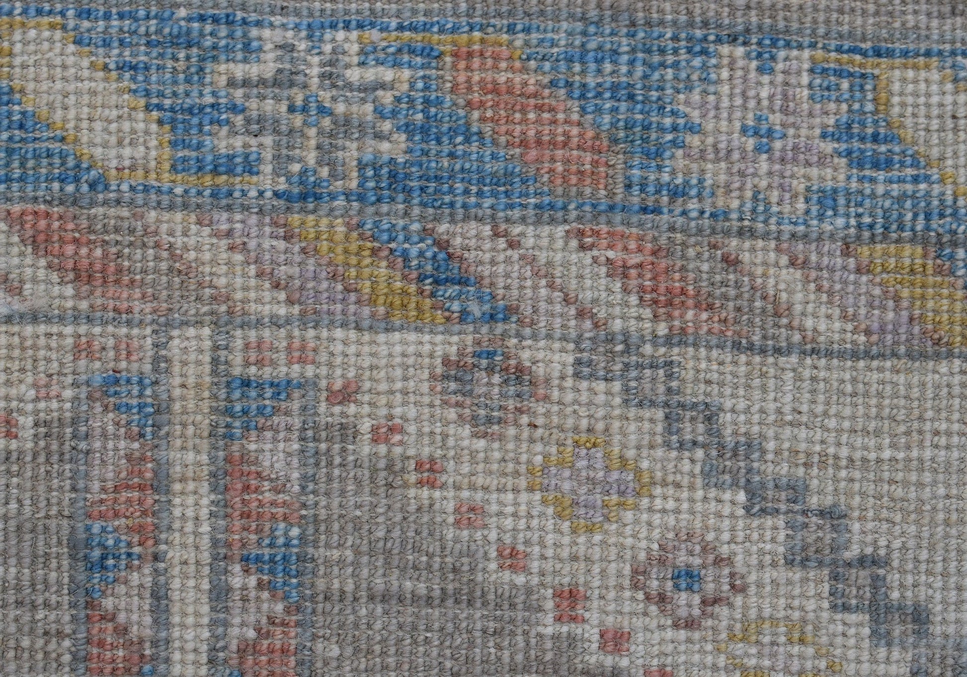 A close-up of a handwoven transitional Oushak runner featuring a geometric floral pattern in blue, pink, and yellow on a neutral background.