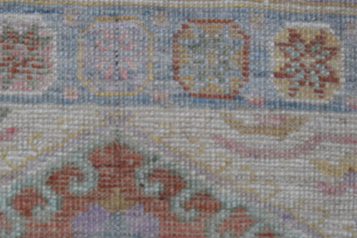 A close-up of a handwoven wool runner rug featuring a floral pattern in muted, transitional tones.