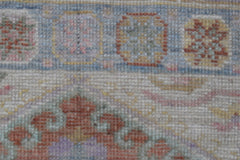 A close-up of a handwoven wool runner rug featuring a floral pattern in muted, transitional tones.