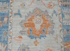 A handwoven wool runner featuring a transitional floral pattern in orange, blue, and beige tones.