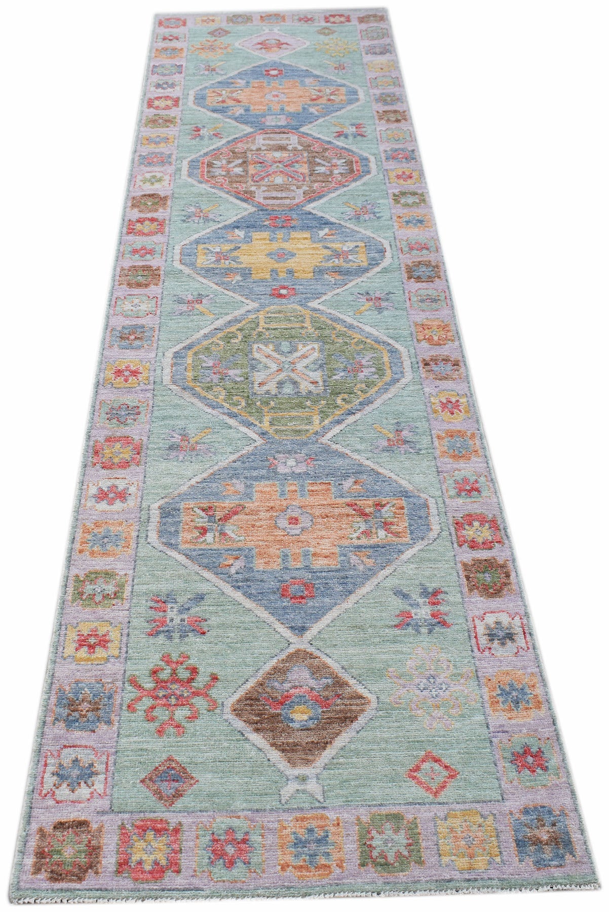 A handwoven transitional Oushak runner featuring geometric diamond motifs on a light green field.