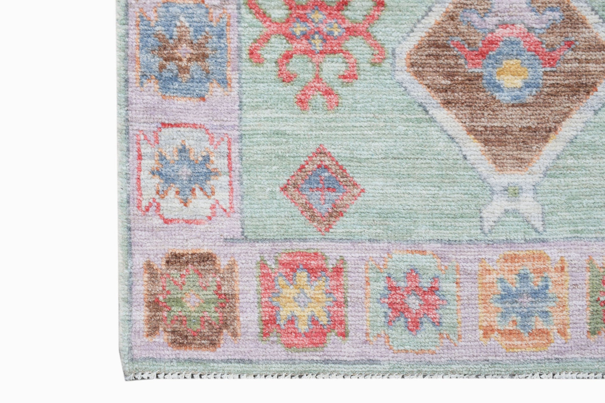 A handwoven wool runner featuring a light green field with colorful geometric and floral motifs.