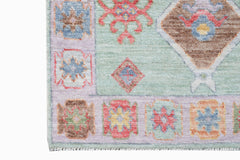A handwoven wool runner featuring a light green field with colorful geometric and floral motifs.