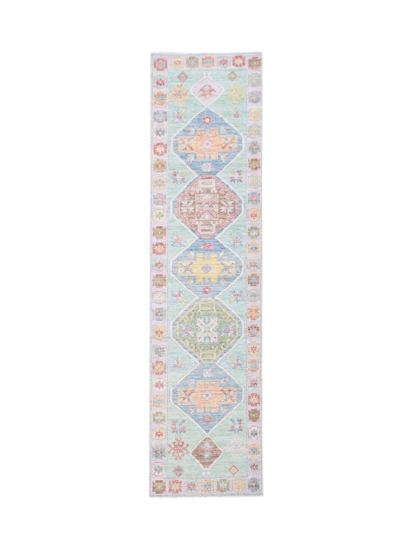 A handwoven wool runner rug featuring a light green background with colorful geometric medallions.