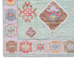 A handwoven wool runner featuring a light green field with geometric floral motifs and a patterned border.