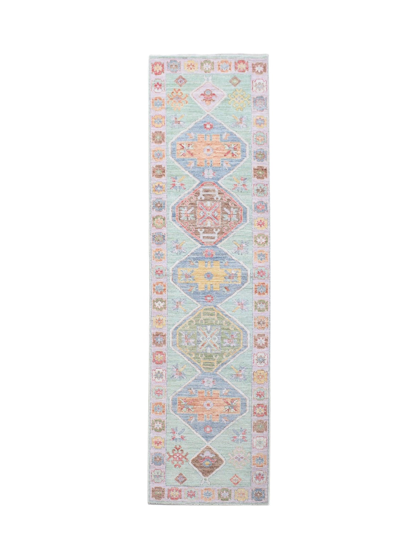 A handwoven wool runner rug featuring a light green field with colorful geometric diamond motifs.