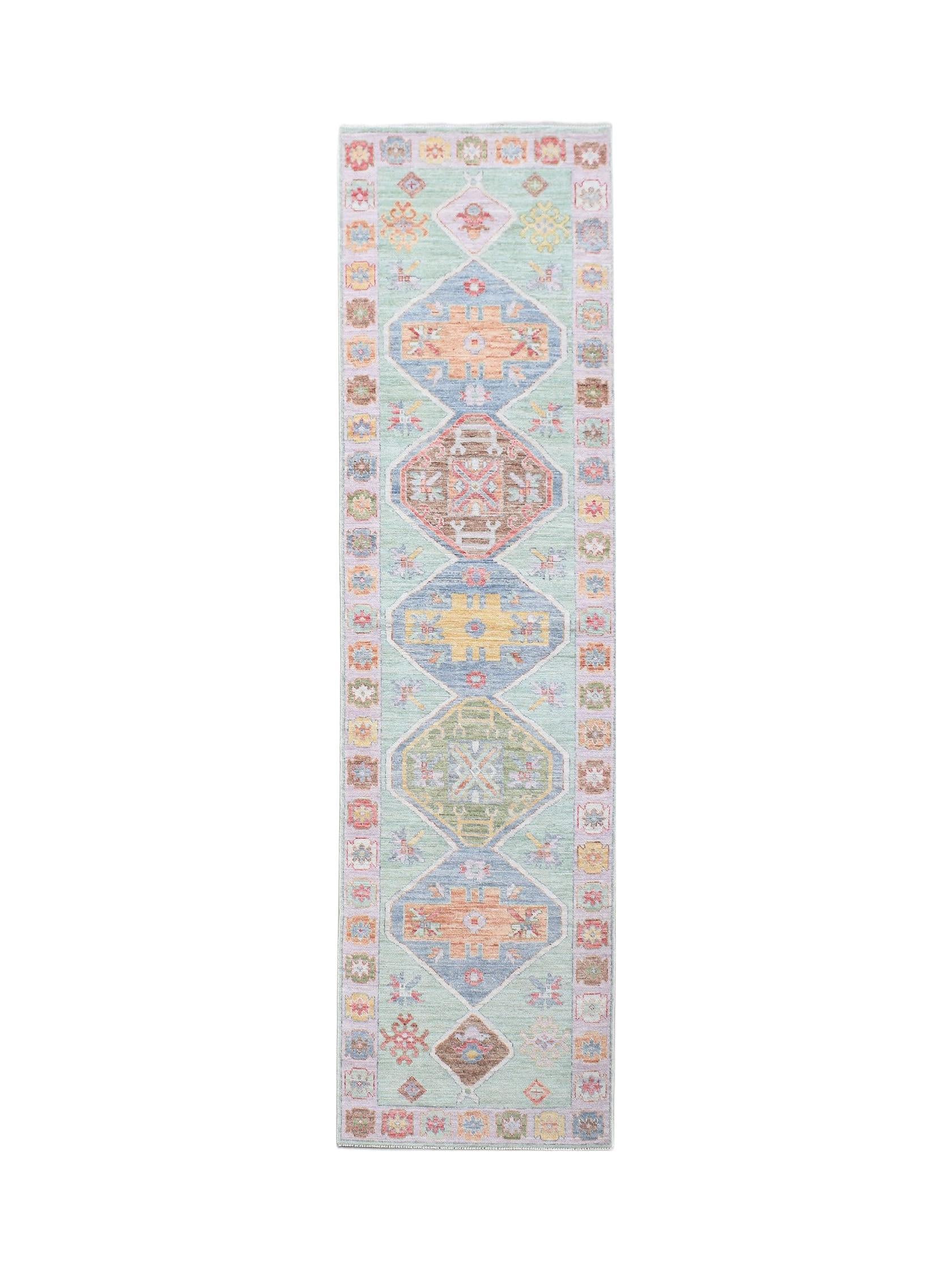A handwoven wool runner rug featuring a light green field with colorful geometric diamond motifs.