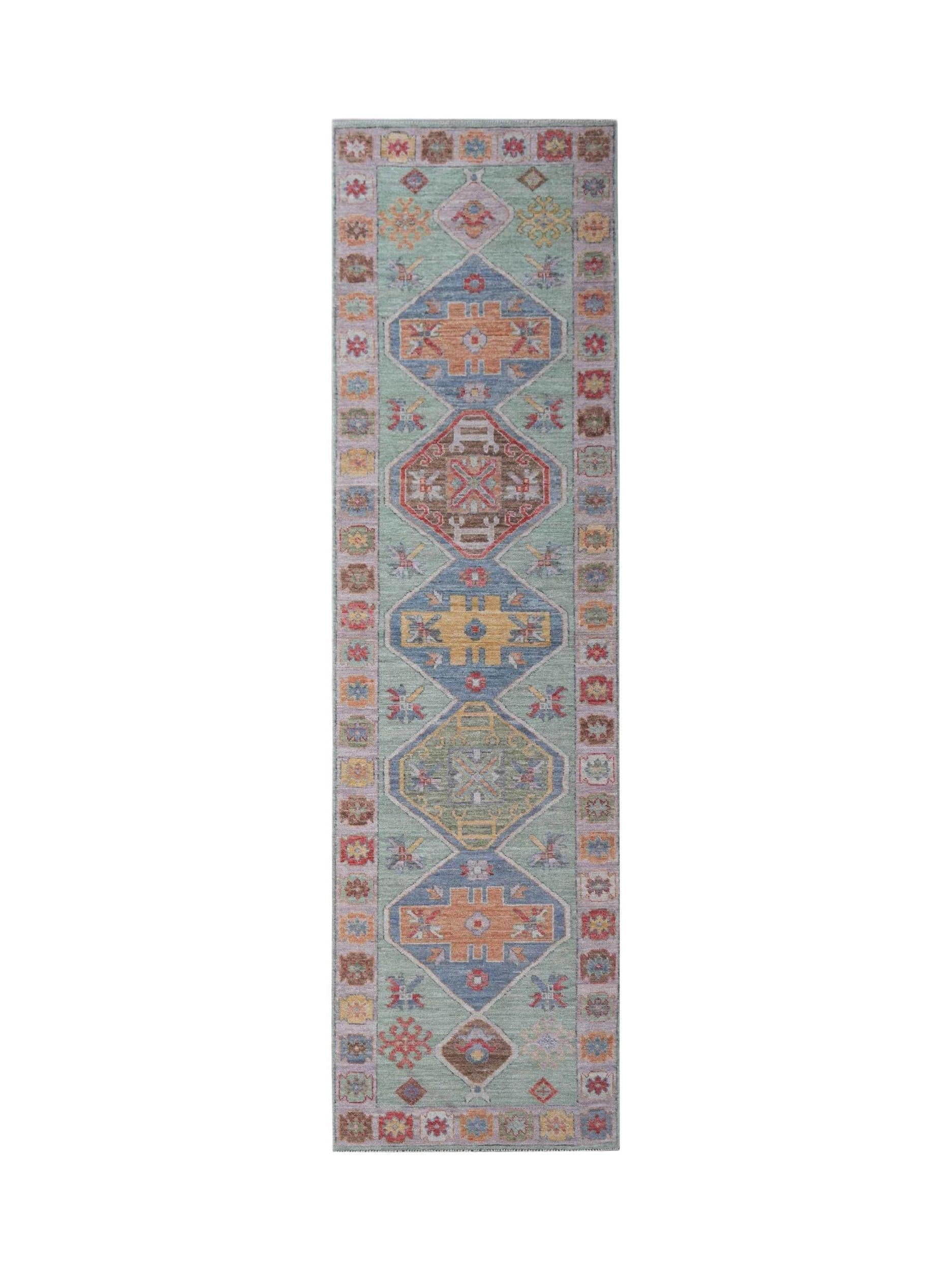 A handwoven wool runner rug featuring a light green field with geometric medallions in muted tones.