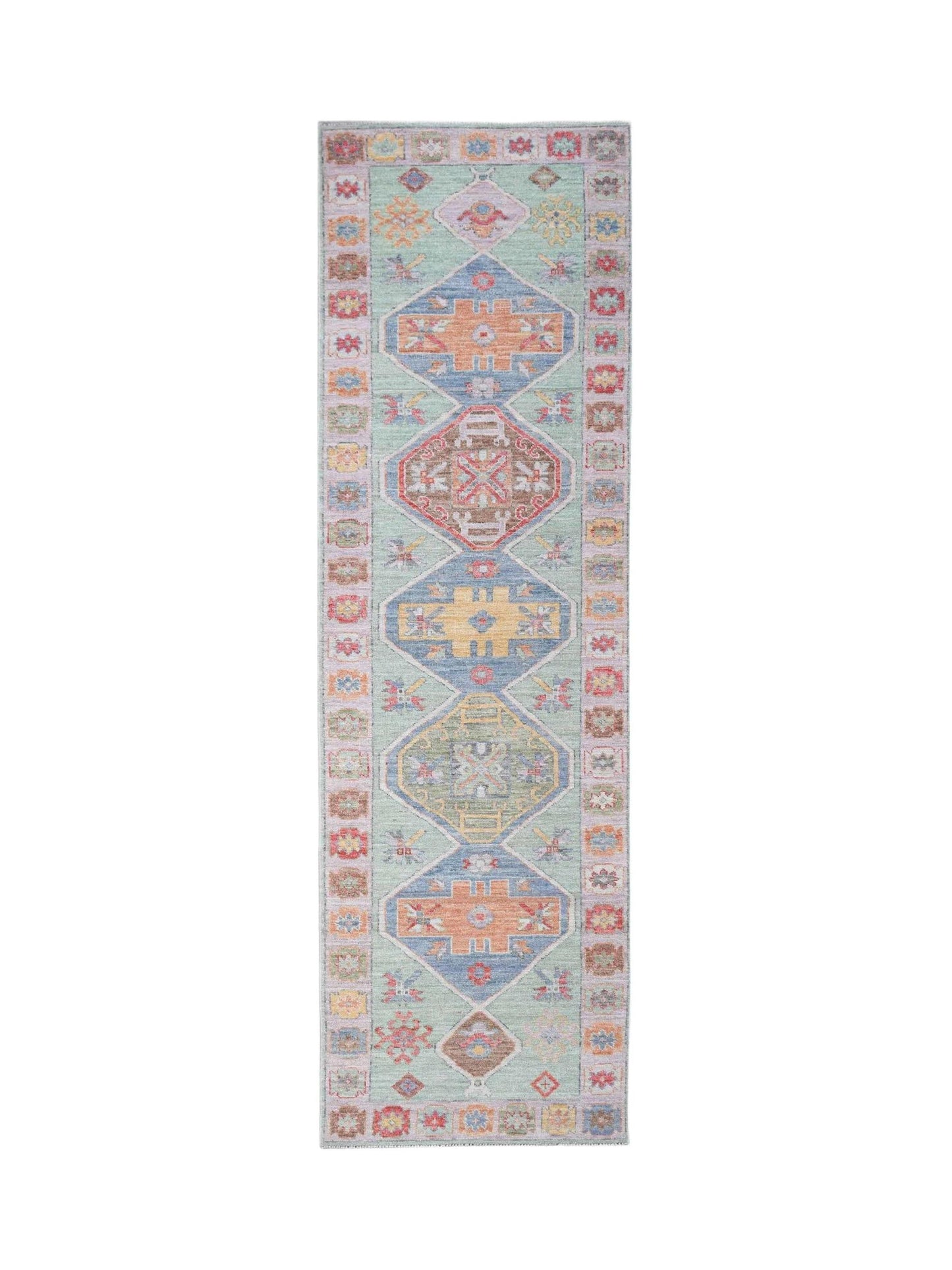 A handwoven wool runner rug featuring a light green field with colorful geometric Oushak motifs.
