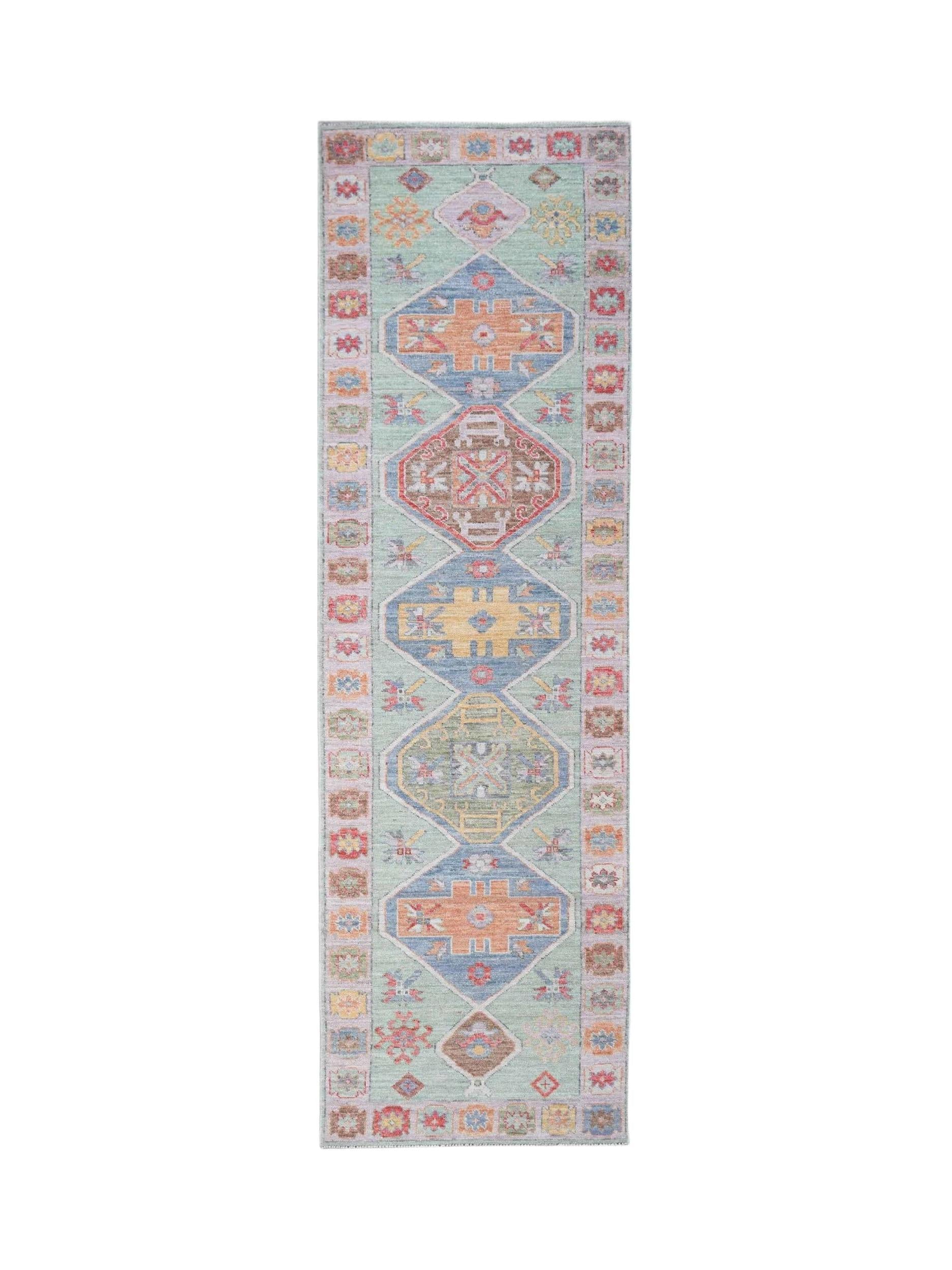 A handwoven wool runner rug featuring a light green field with colorful geometric Oushak motifs.