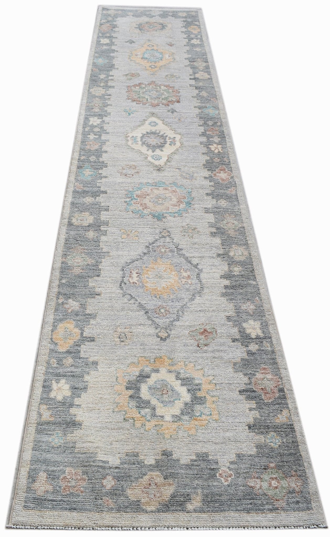 A handwoven transitional Oushak runner rug featuring a grey field with floral and geometric motifs.