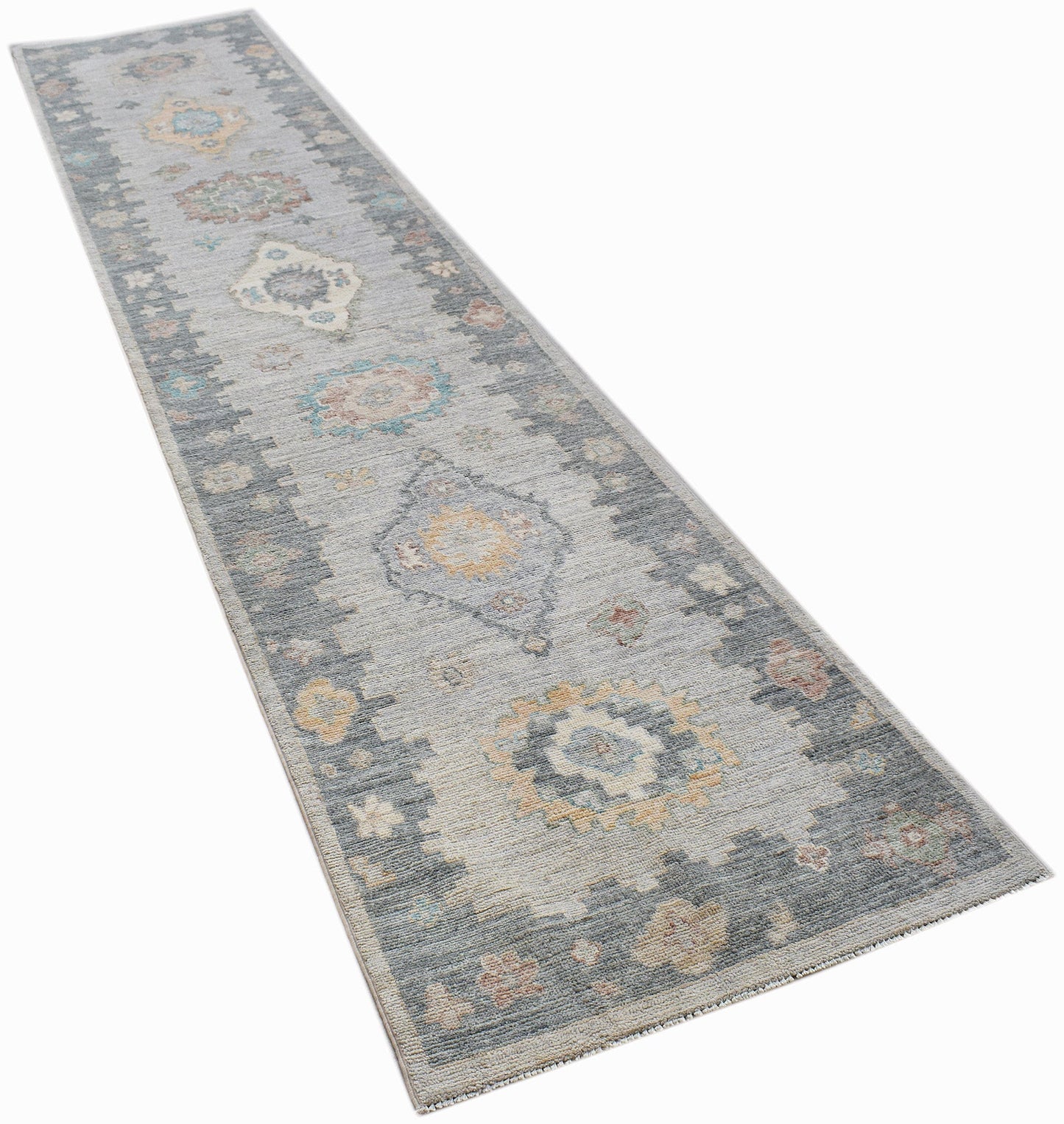 A handwoven wool runner rug featuring a transitional Oushak pattern in grey and muted tones.