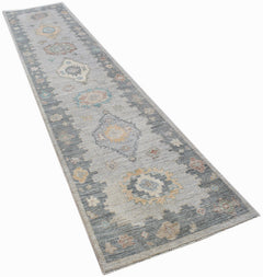 A handwoven wool runner rug featuring a transitional Oushak pattern in grey and muted tones.