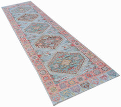 A handwoven wool runner rug featuring a light blue field with repeating geometric floral motifs.