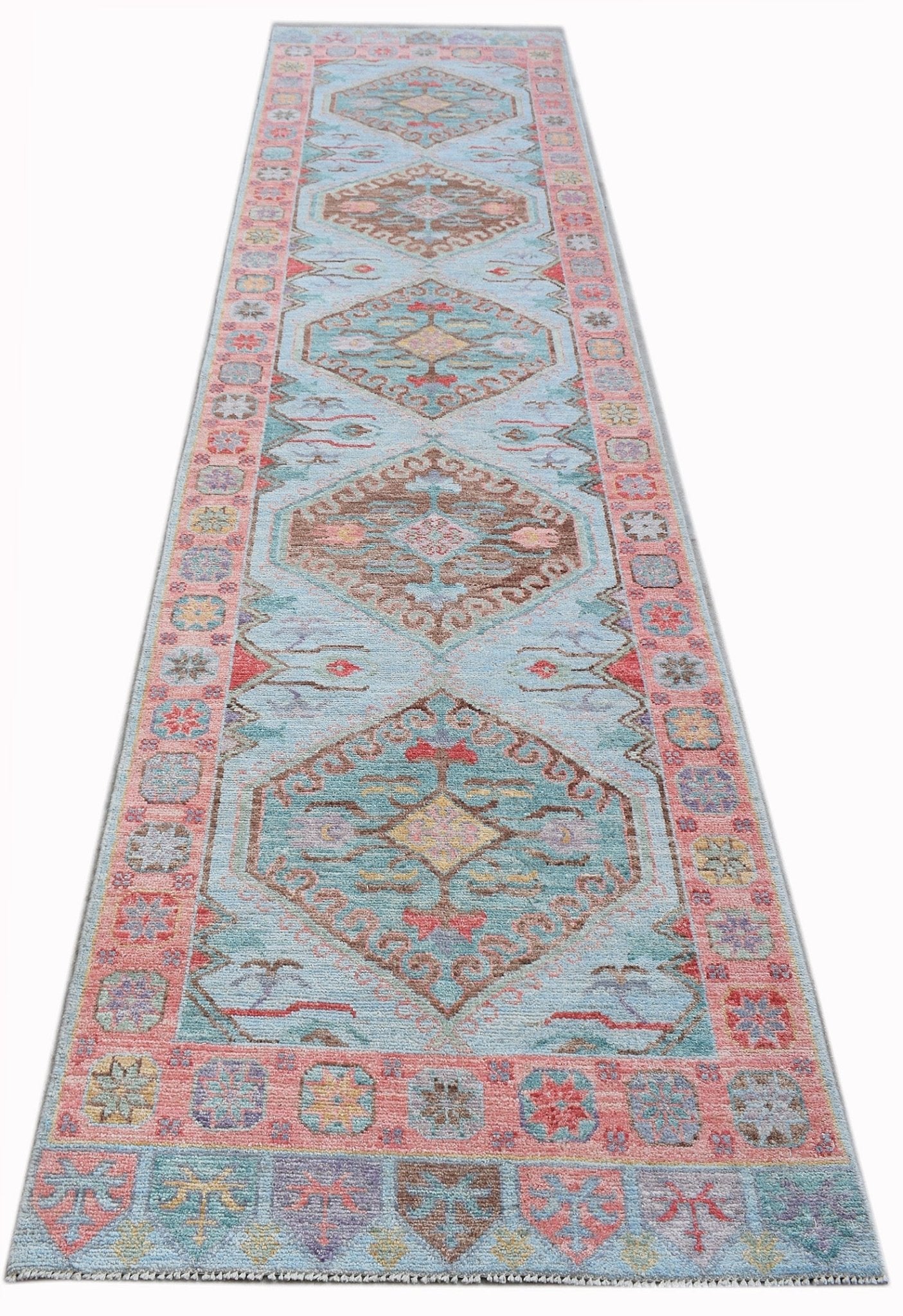 A handwoven wool runner rug featuring a light blue field with repeating geometric floral medallions.