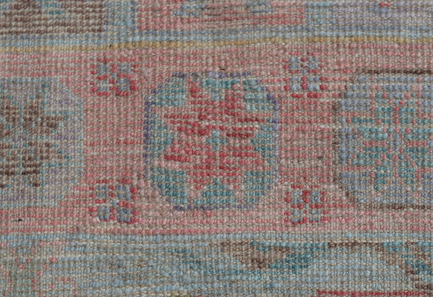 A close-up of a handwoven wool runner rug featuring a faded geometric pattern in pink and blue.