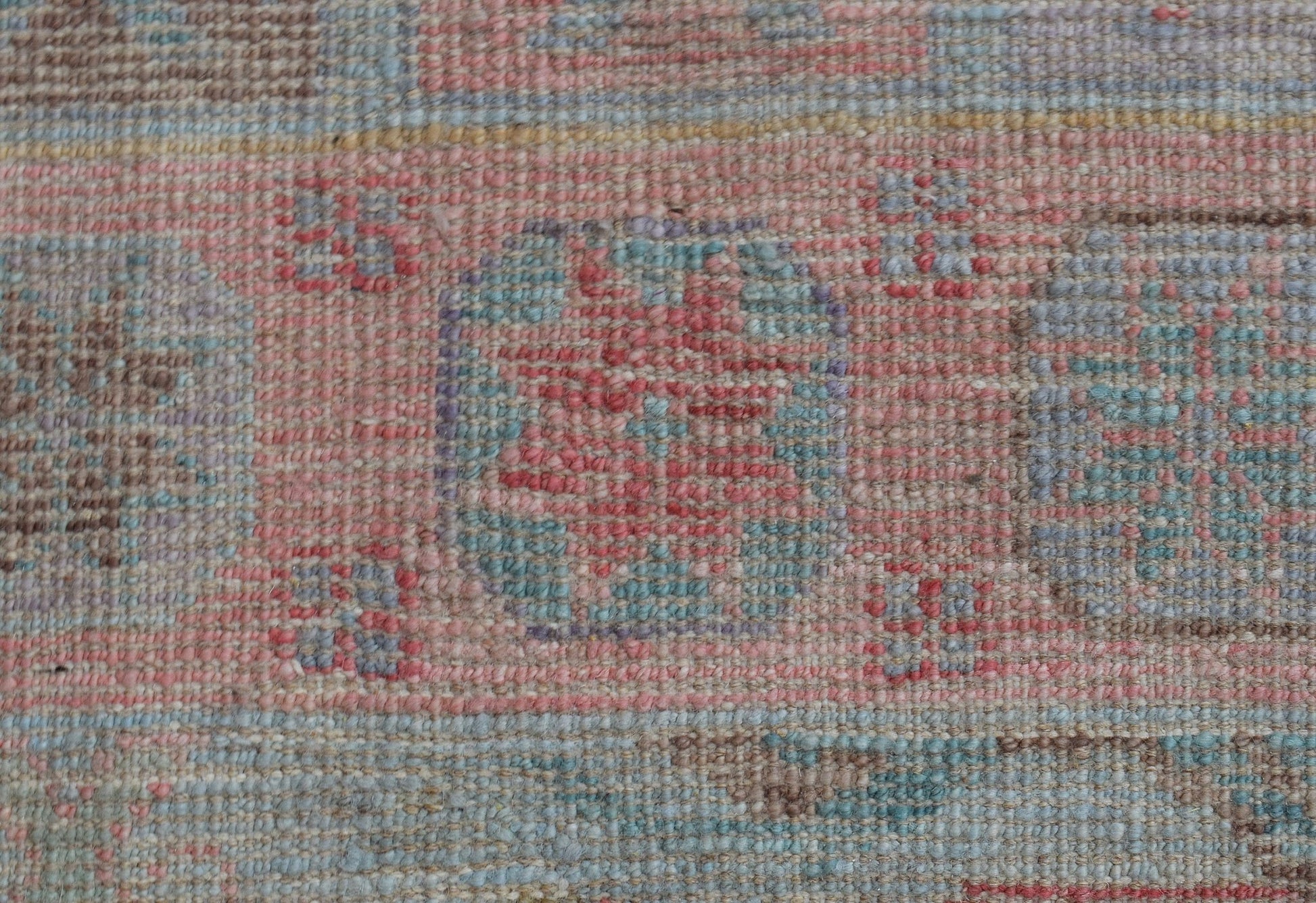 A close-up of a handwoven wool runner rug featuring a faded geometric pattern in pink and blue.