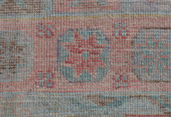 A close-up of a handwoven wool runner rug featuring a faded geometric pattern in pink and blue.