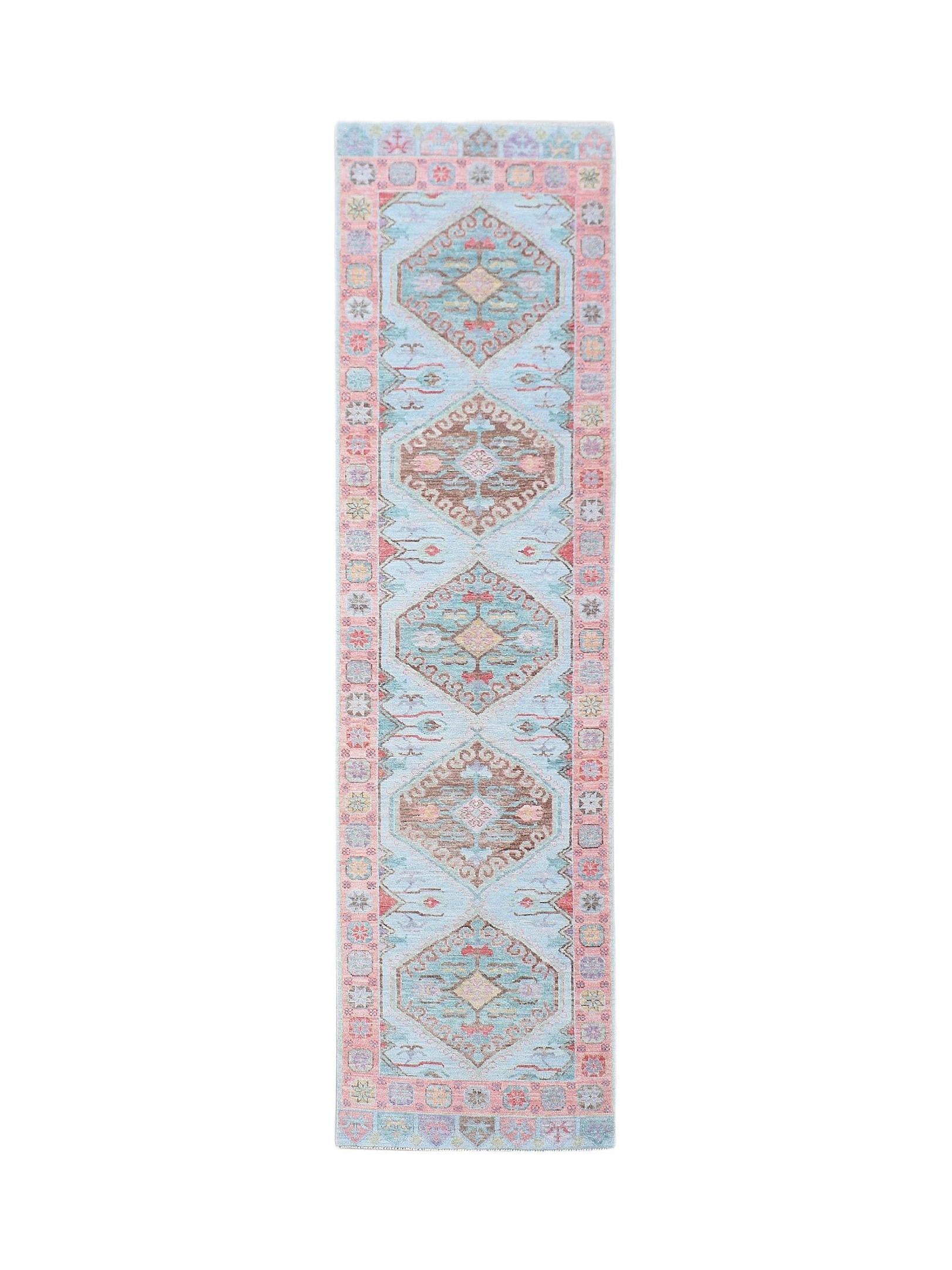 A handwoven wool runner rug featuring a light blue field with repeating geometric floral medallions.