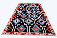 A handmade wool rug featuring a geometric pattern of blue, red, and cream diamonds on black.