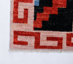 A handmade wool rug featuring a geometric red and black pattern on a soft pink background.