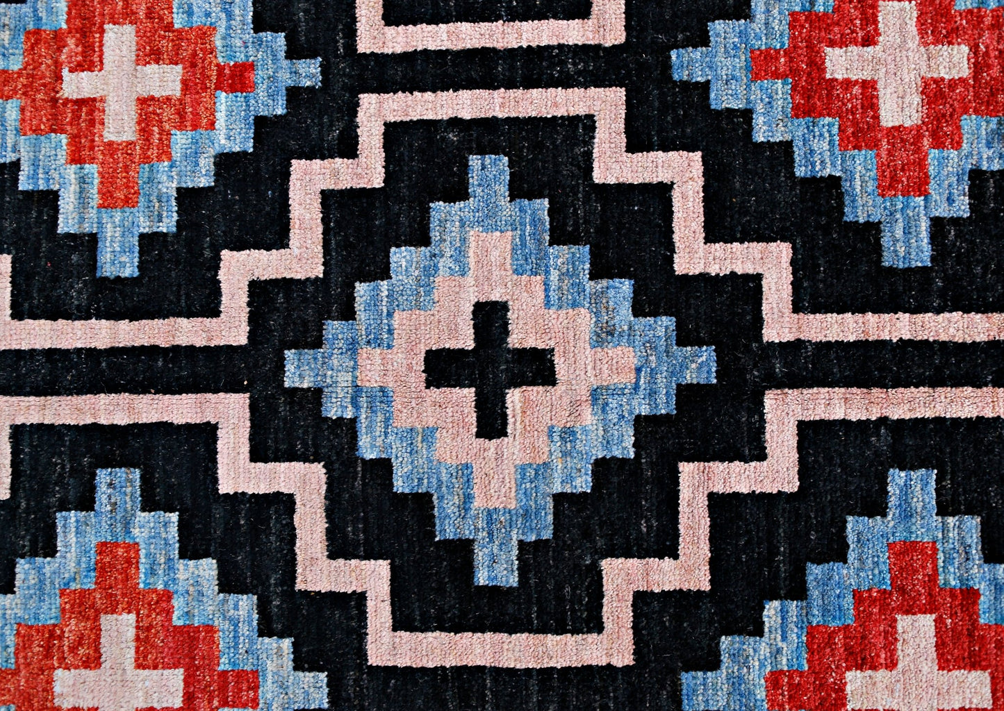 A handmade wool rug featuring a geometric pattern of black, blue, pink, and red diamond motifs.