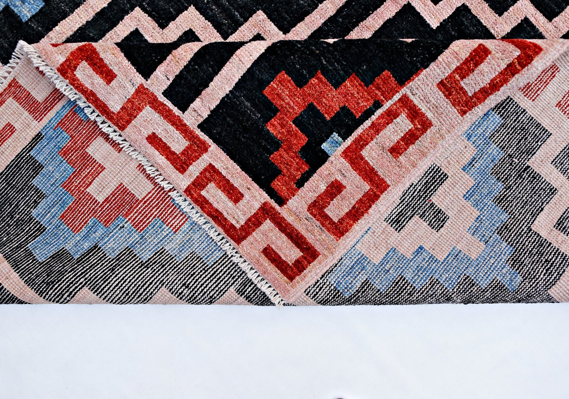 A handmade wool rug from Afghanistan featuring a geometric pattern in red, blue, black, and cream.