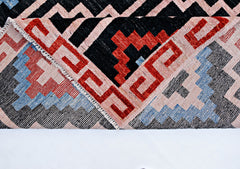 A handmade wool rug from Afghanistan featuring a geometric pattern in red, blue, black, and cream.