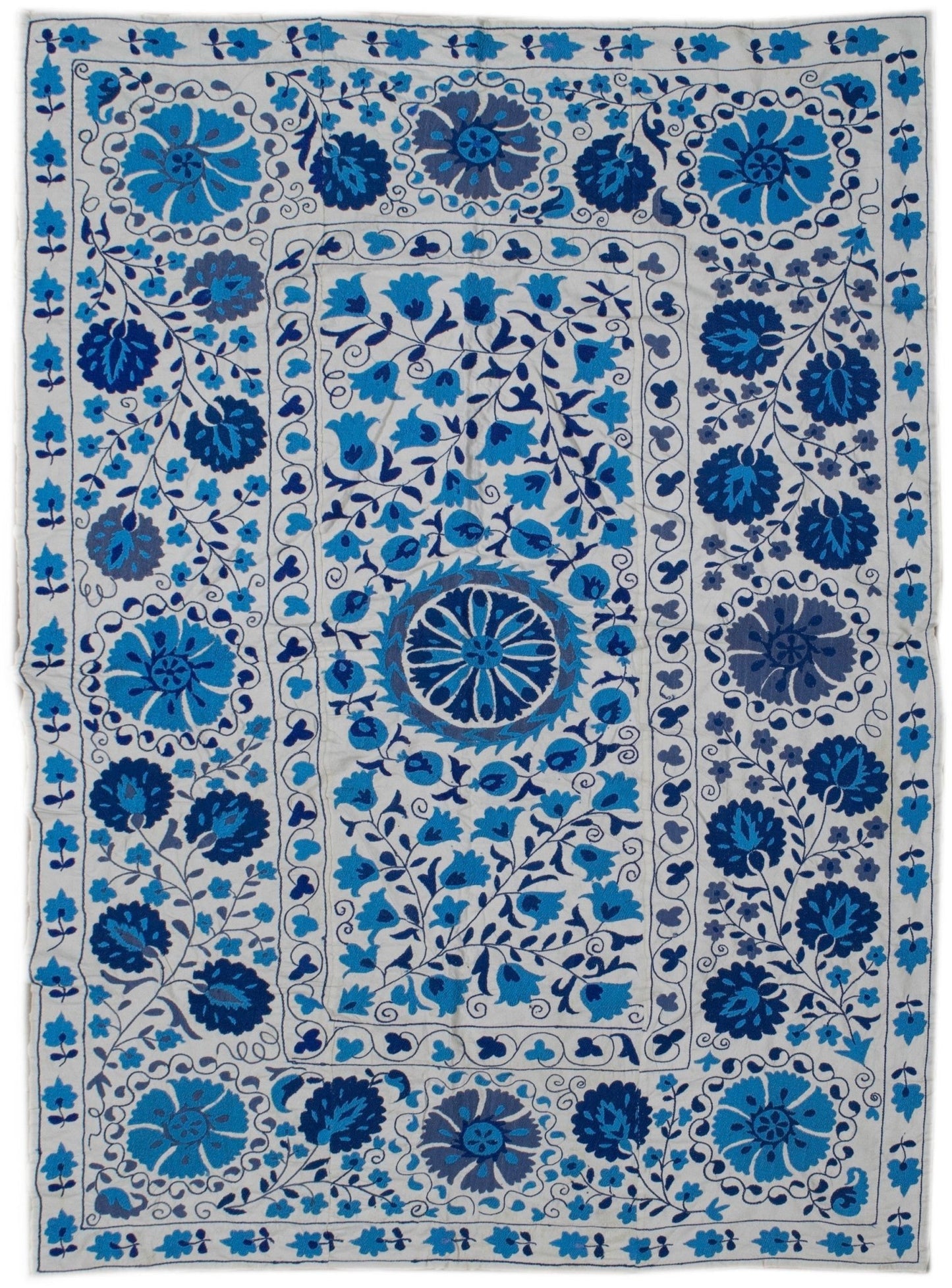 Handmade Uzbek suzani featuring intricate blue floral embroidery on a white cotton base.