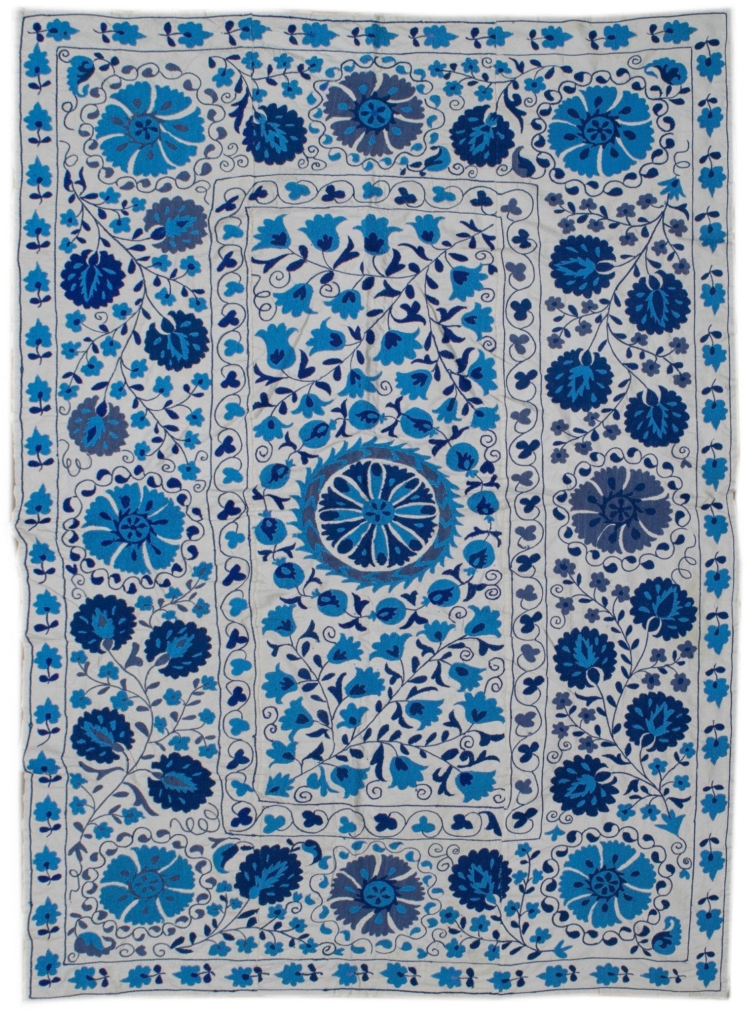 Handmade Uzbek suzani featuring intricate blue floral embroidery on a white cotton base.