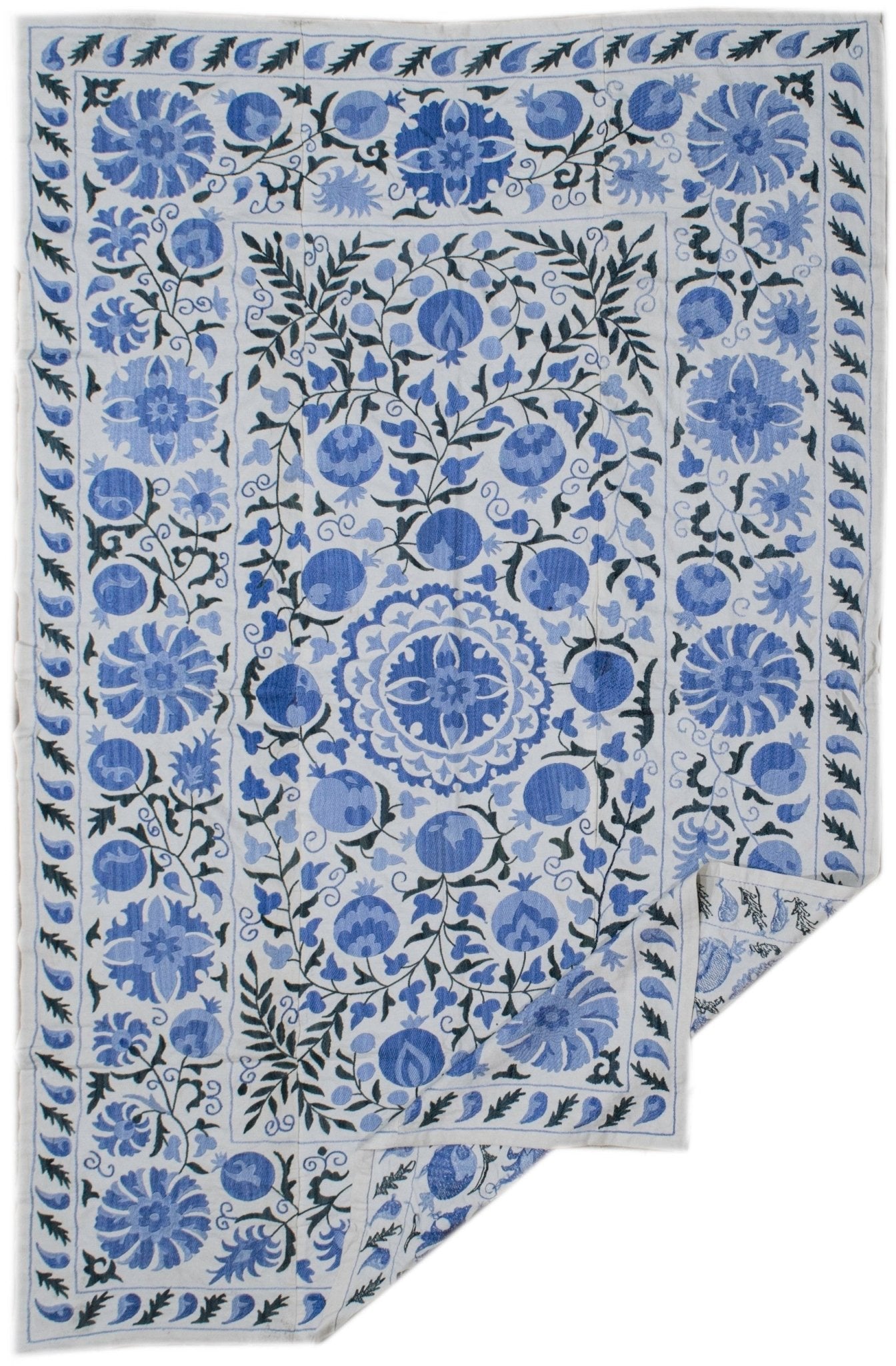 Hand-embroidered Uzbek suzani featuring blue floral and pomegranate motifs on a white cotton base.