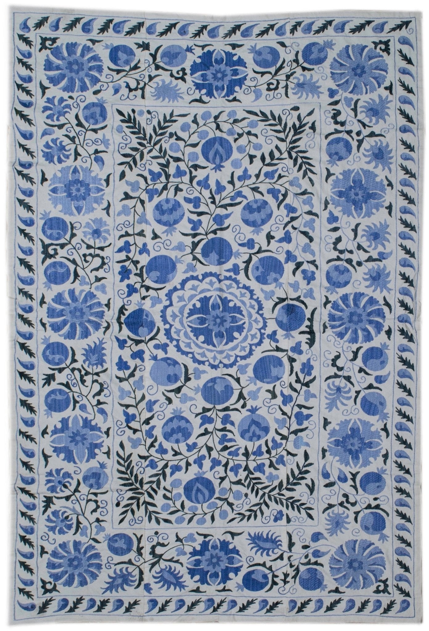 A rectangular Uzbek suzani featuring blue floral and pomegranate embroidery on a white cotton base.